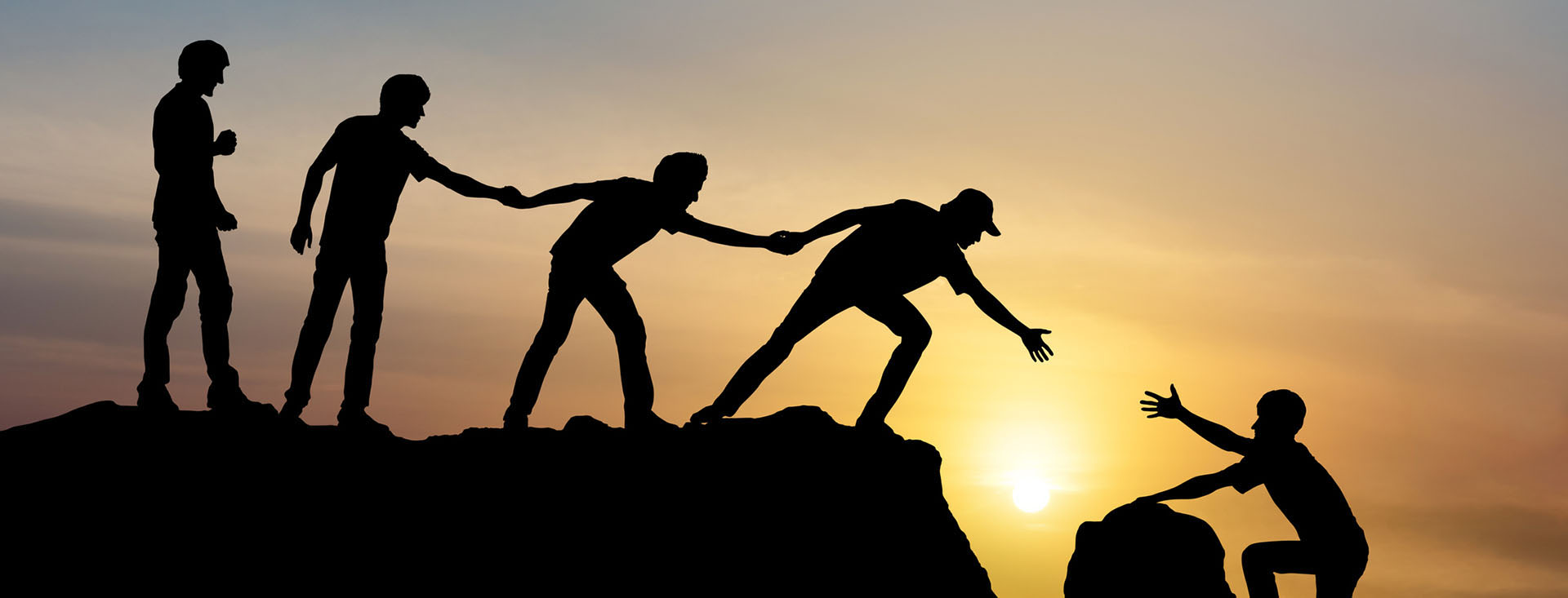Die Silhouette zeigt vier Personen auf einem Felsen, die sich an den Händen halten und einer fünften Person die Hand reichen, die einen kleineren Felsen hochklettert